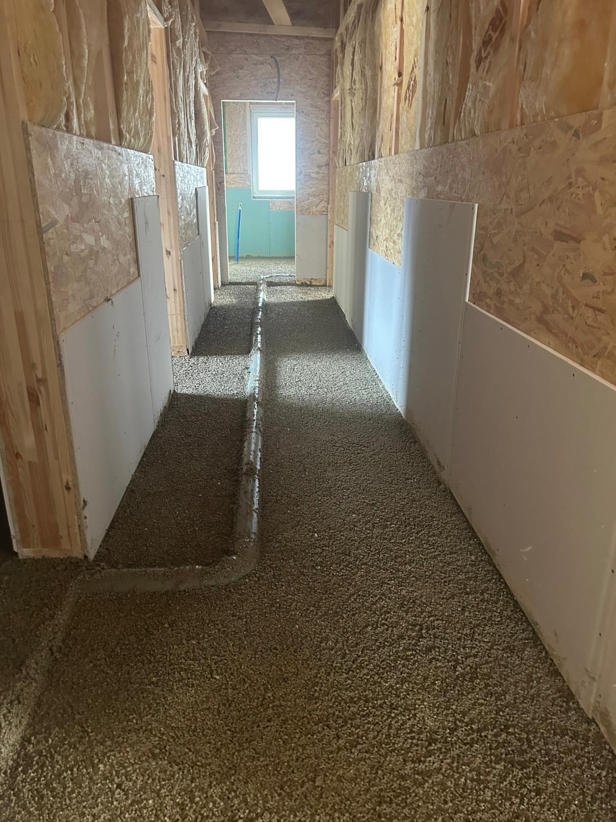 Innenflur im Bau mit noch nicht fertiggestellten Wänden und Fußböden, der zu einer Tür führt.
