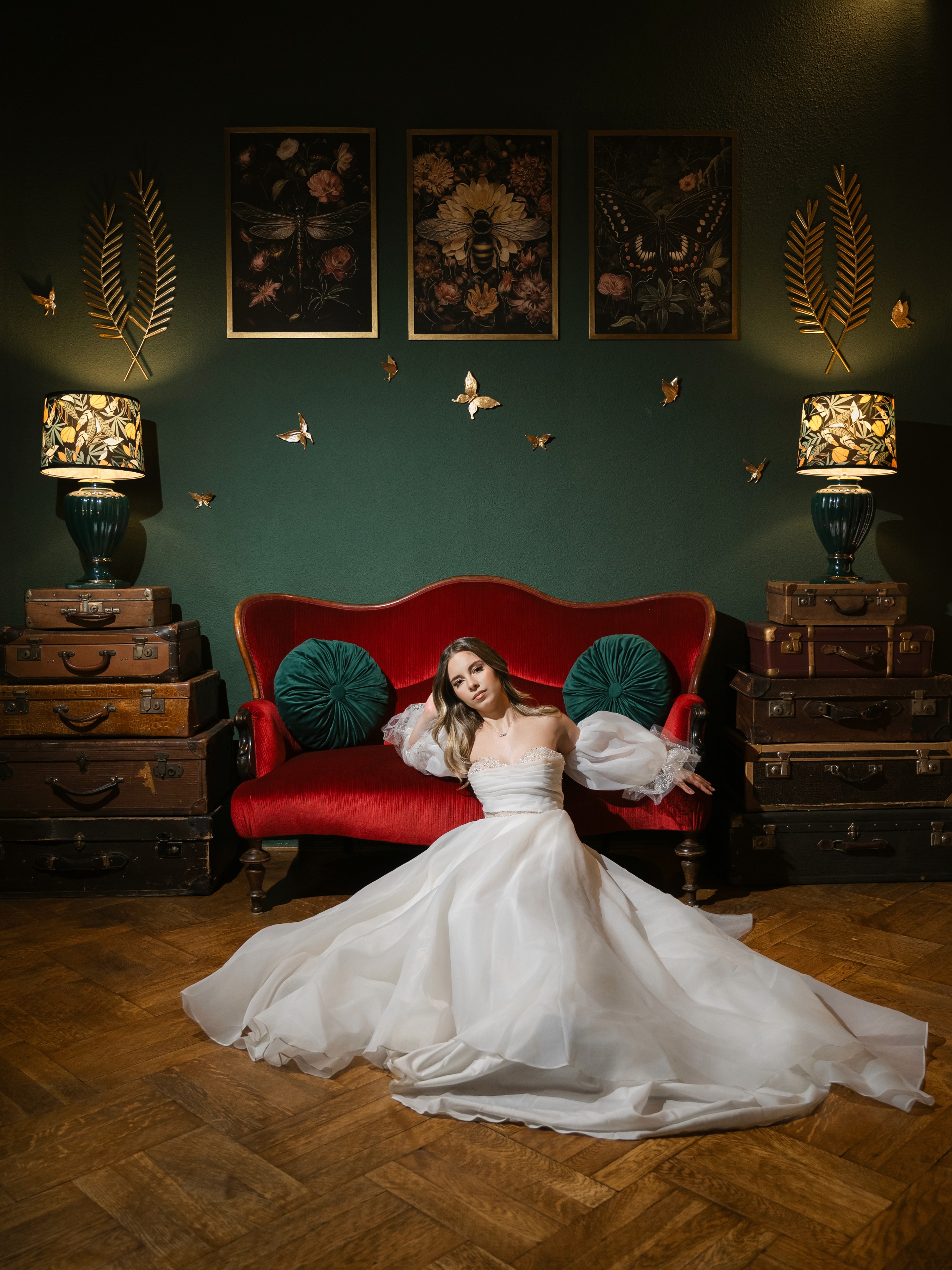 Mireasă singură pe canapea roșie, decor verde închis, rochie albă amplă, fotografie documentară nuntă
