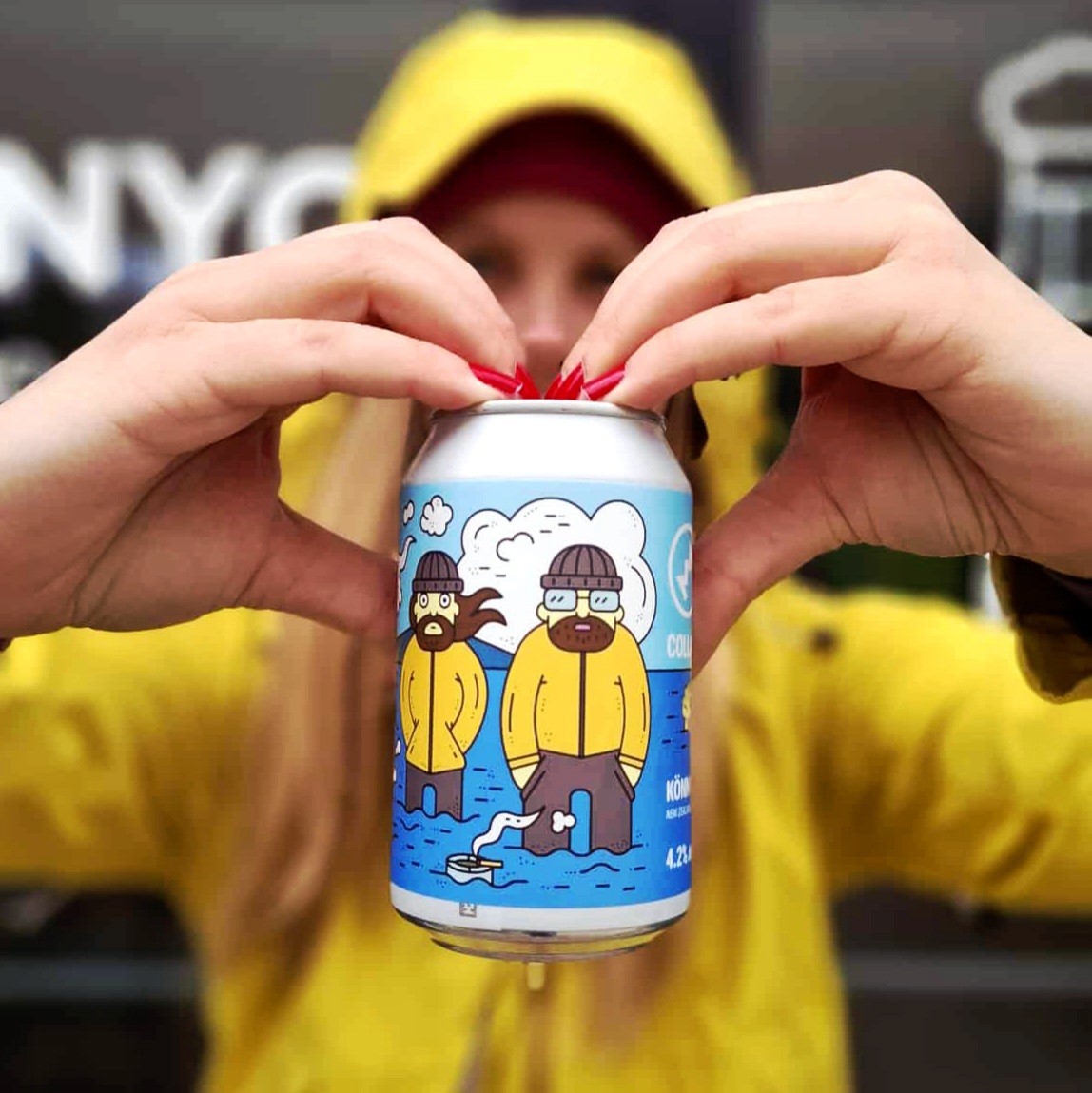 Woman in blue hat and sweater sitting on couch with laptop.
