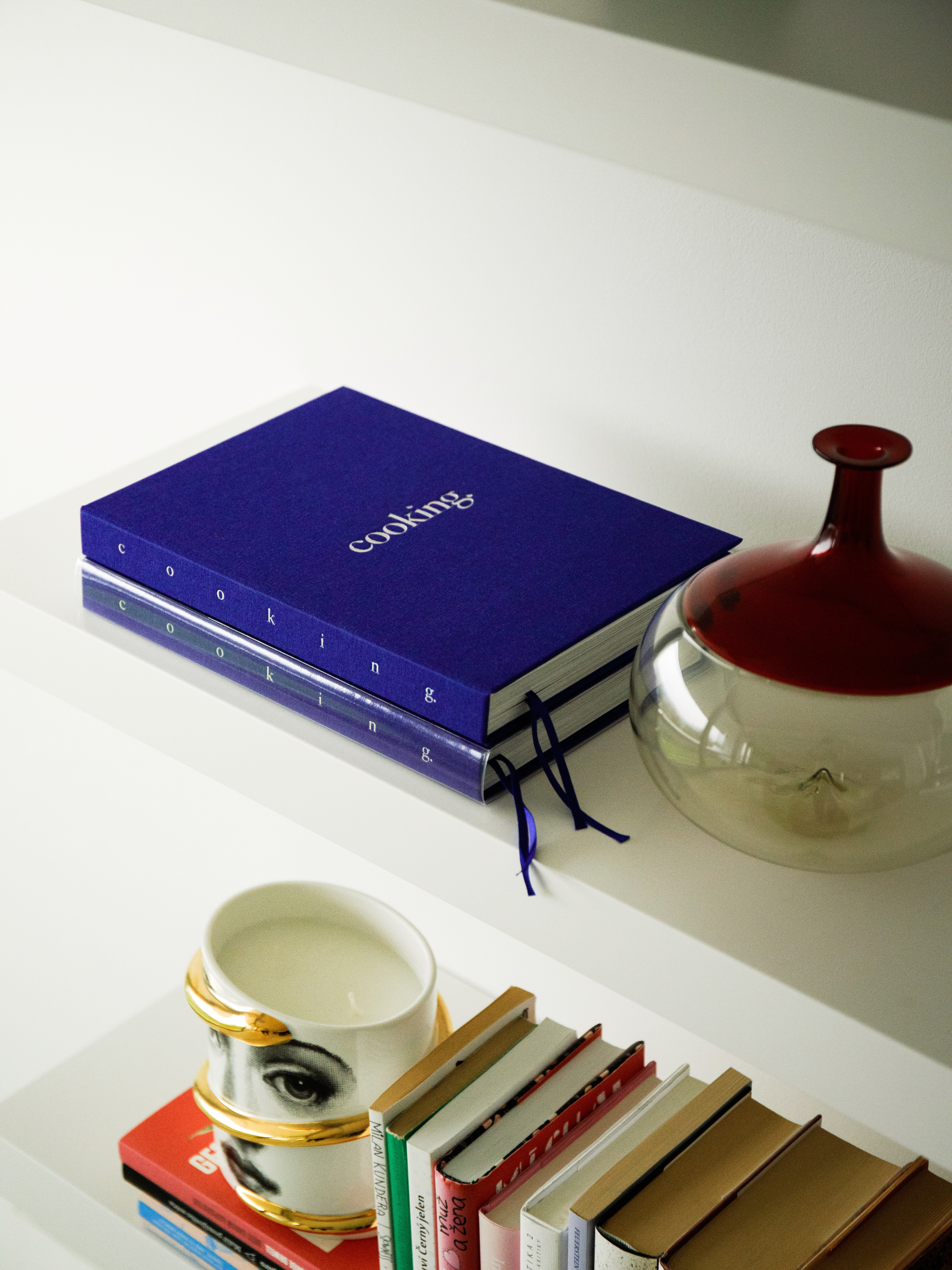 Still life of a blue cookbook by Cooking with Kristiana, ceramic vessels, and porcelain cup on a neutral surface — quiet elegance.