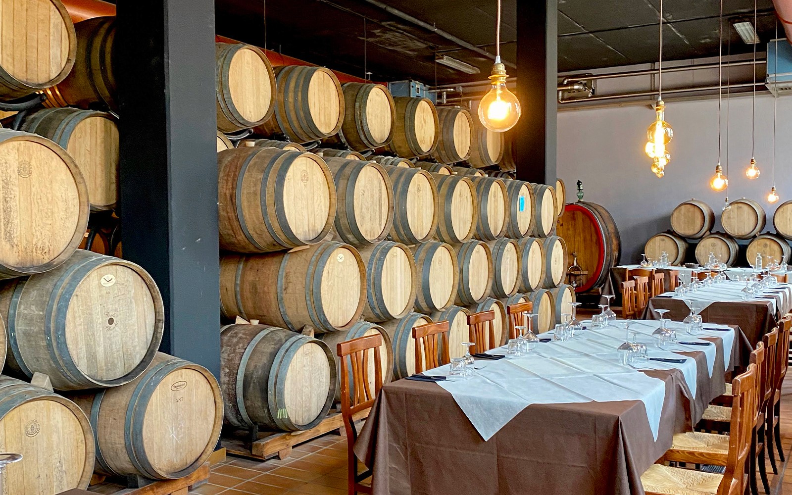 Sala de degustação da vinícola Chianti com barris de madeira e mesas de jantar montadas.