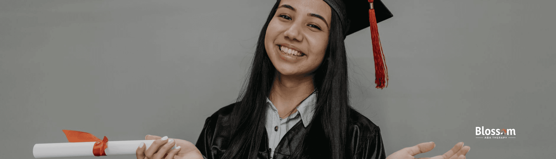 A smiling BCBA bachelor's degree graduate in a cap and gown holding a diploma in Nebraska.