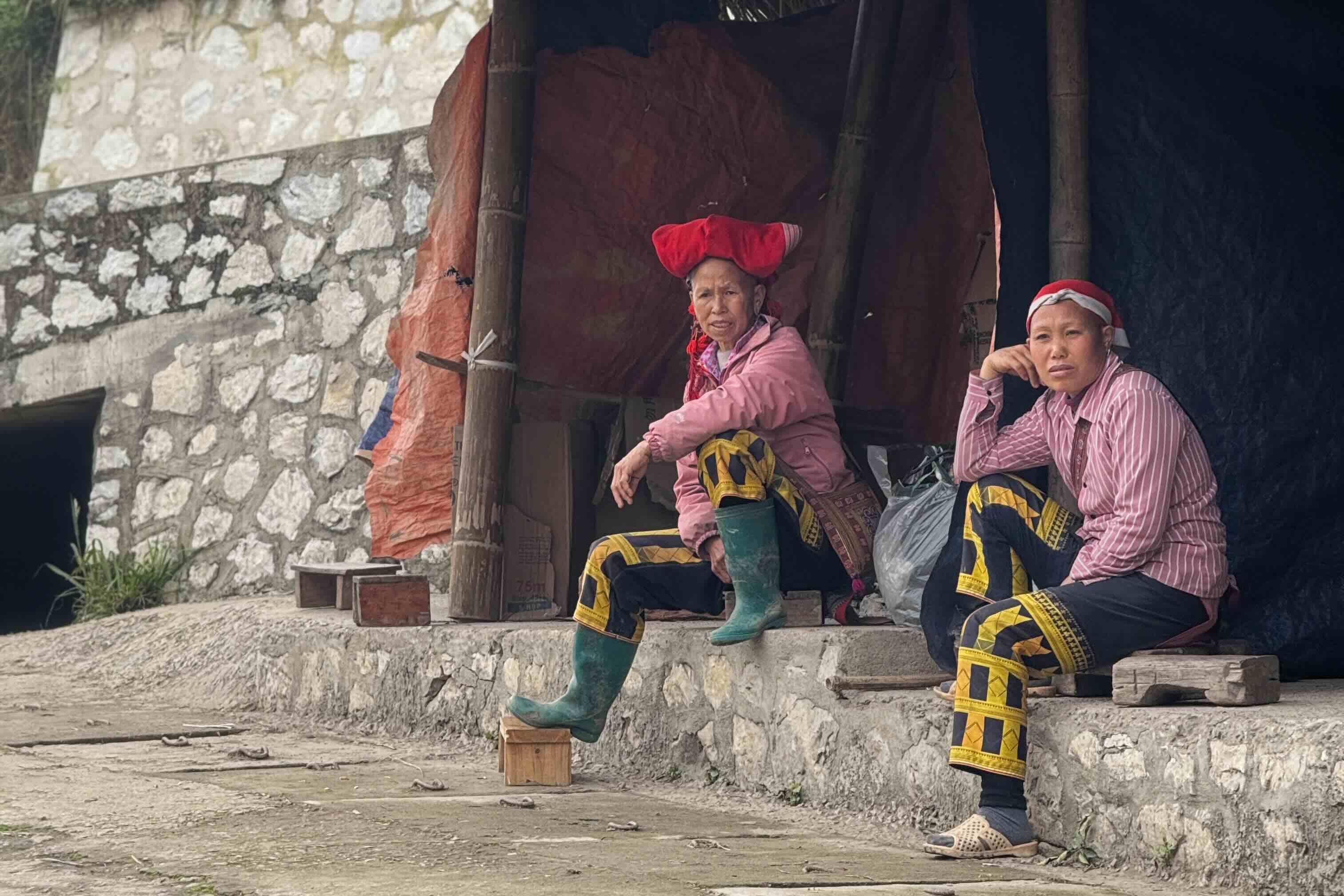 Red Dao women in traditional clothing sitting outside a house in Ta Phin village near Sapa