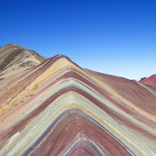 一座山下在晴朗的藍天之下，有著五顏六色的紅色、黃色和藍色條紋層。