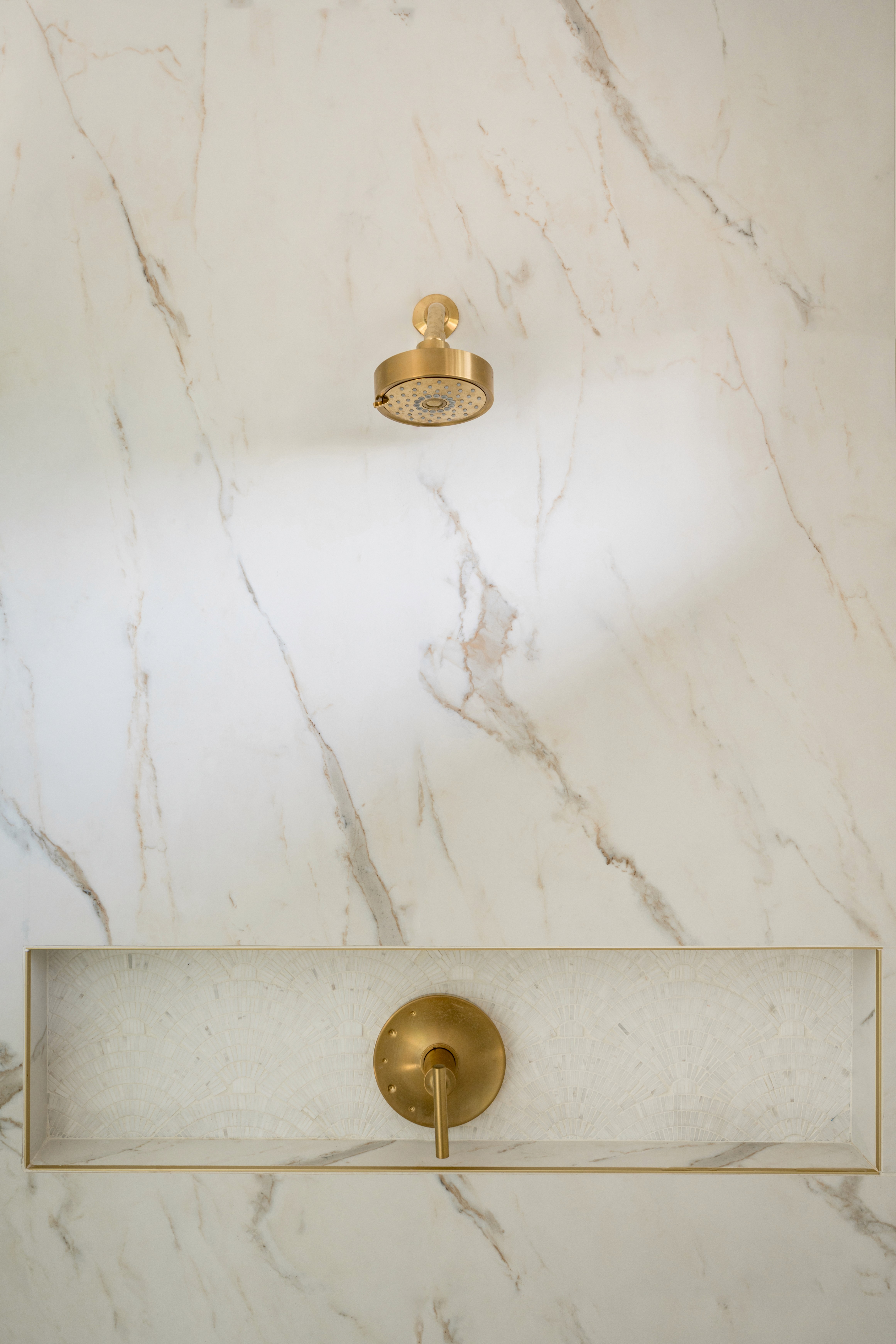 A luxurious primary bathroom adorned with marble accents, a double vanity with modern fixtures, and a glass-enclosed rainfall shower. Soft neutral tones and elegant finishes create a serene, spa-like atmosphere, perfect for relaxation by Jubilee Interiors in Lakewood, California