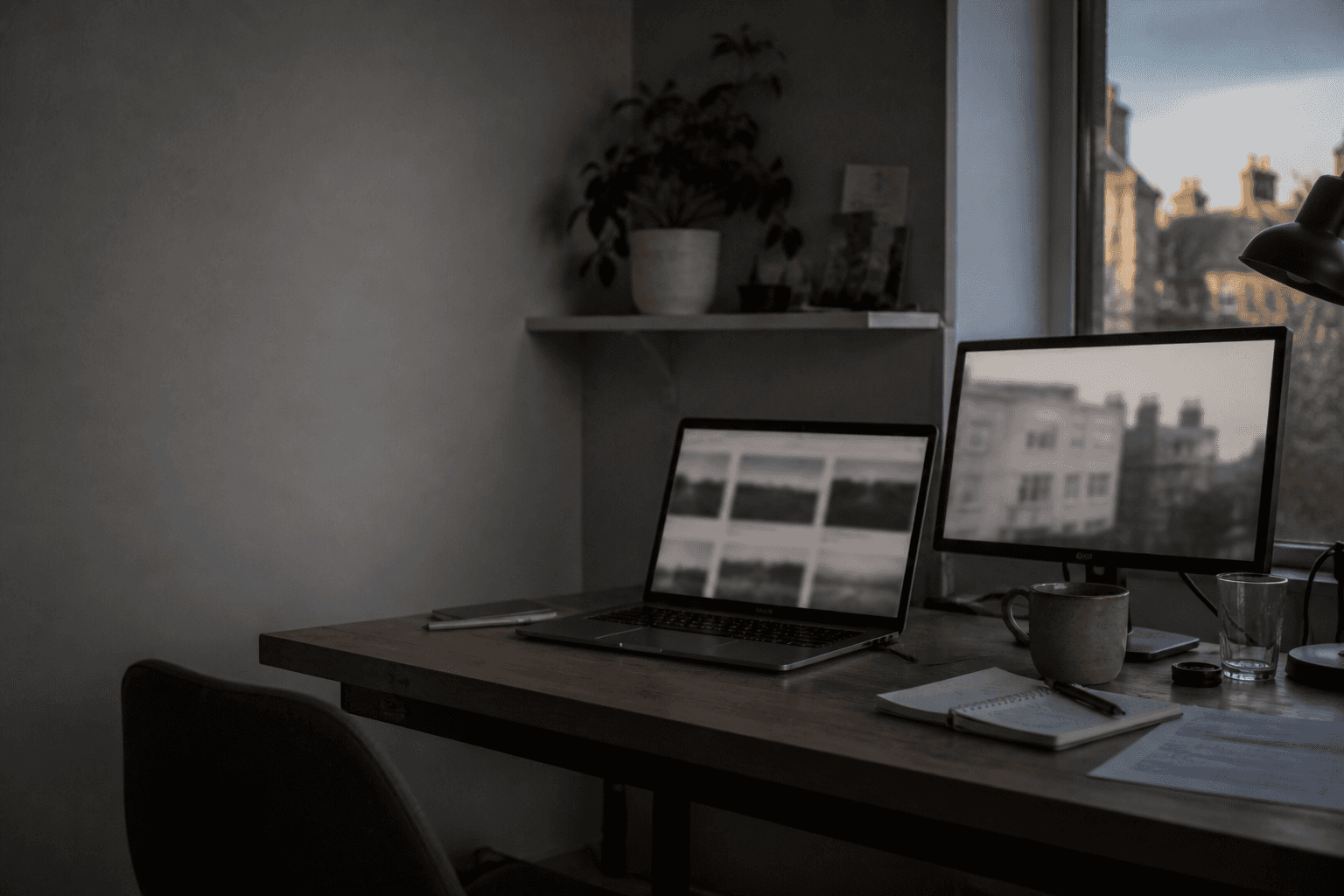 Indoor workspace in Cambridge with a laptop and monitor on a desk, softly lit by window light.