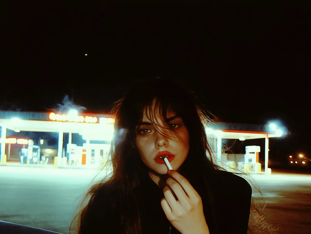 A person at night in front of a blurred, glowing diner or gas station with warm neon lights.