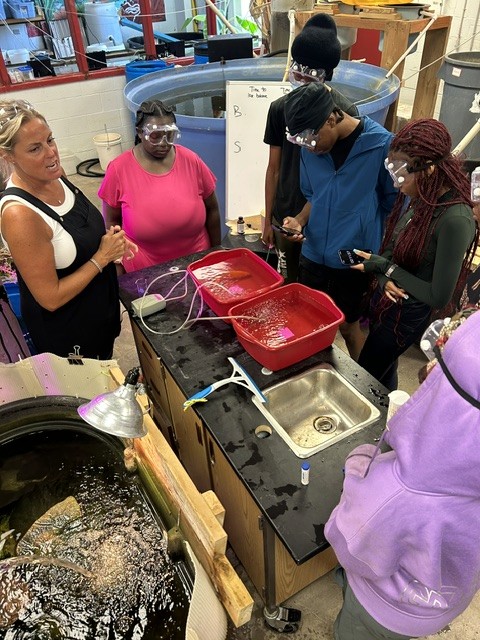 Students in safety goggles testing water samples at an aquaponics lab bench