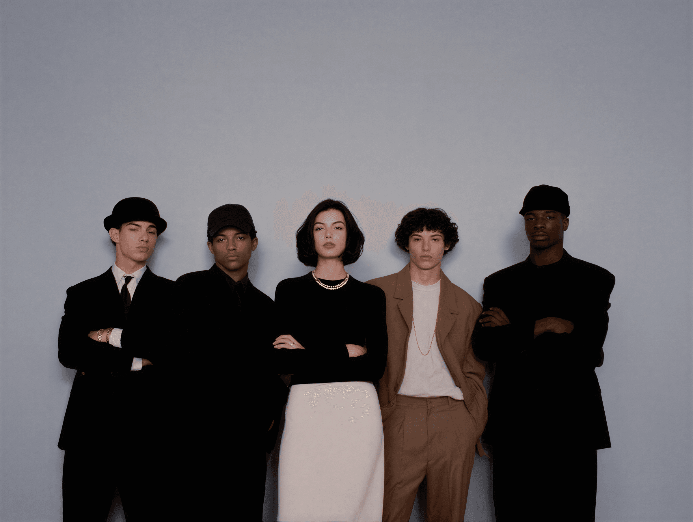 Five people in fashionable attire stand against a light blue background.