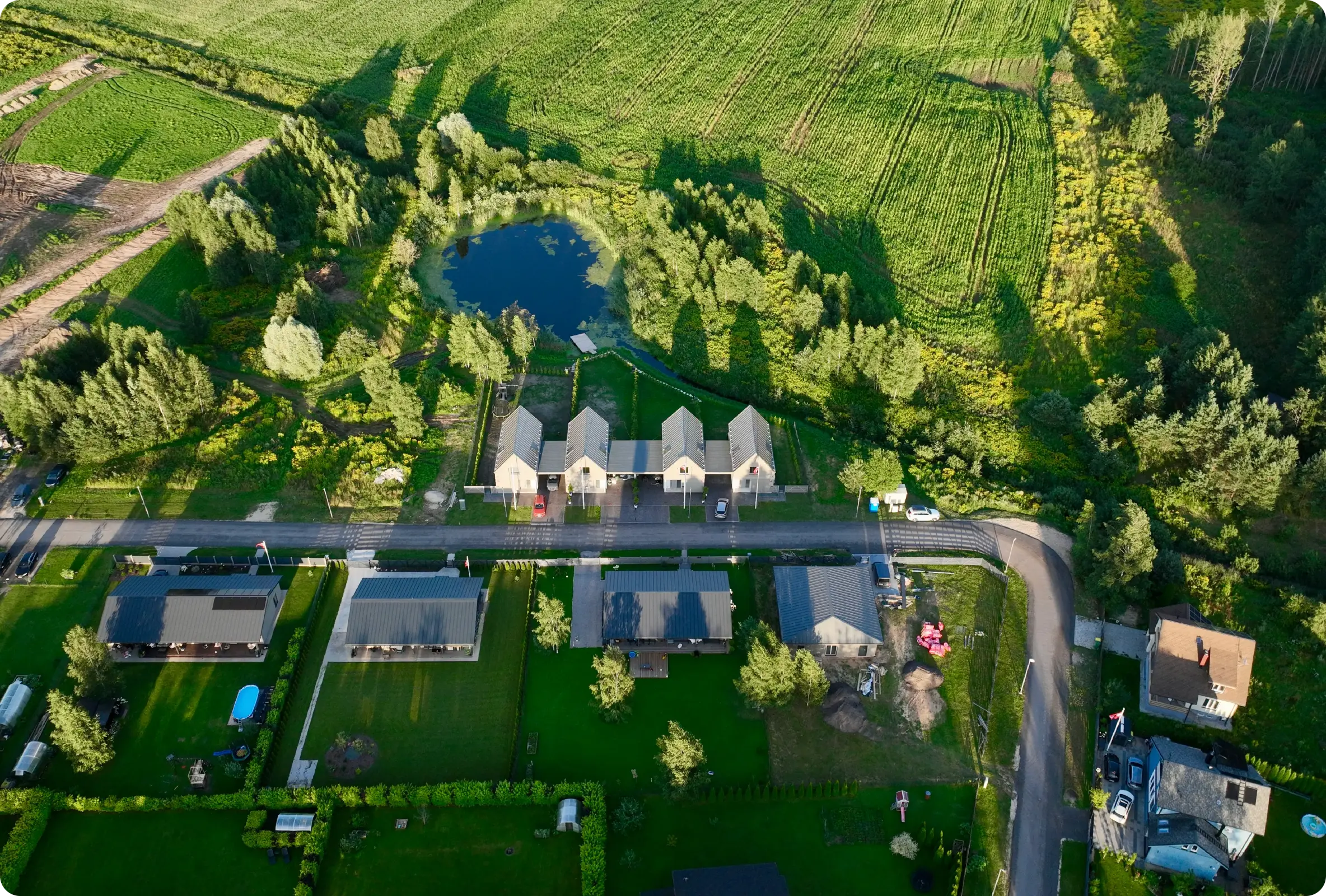 Aerial drone view of a rural construction site with houses, a pond, and green farmland