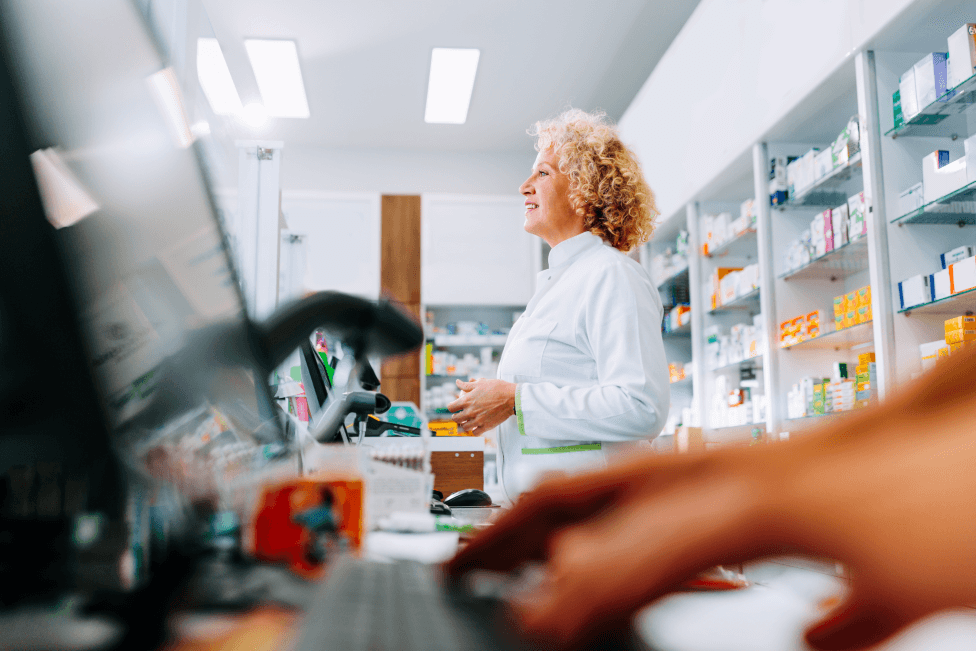 A woman stands behind the counter in a pharmacy, ready to assist customers with their needs.