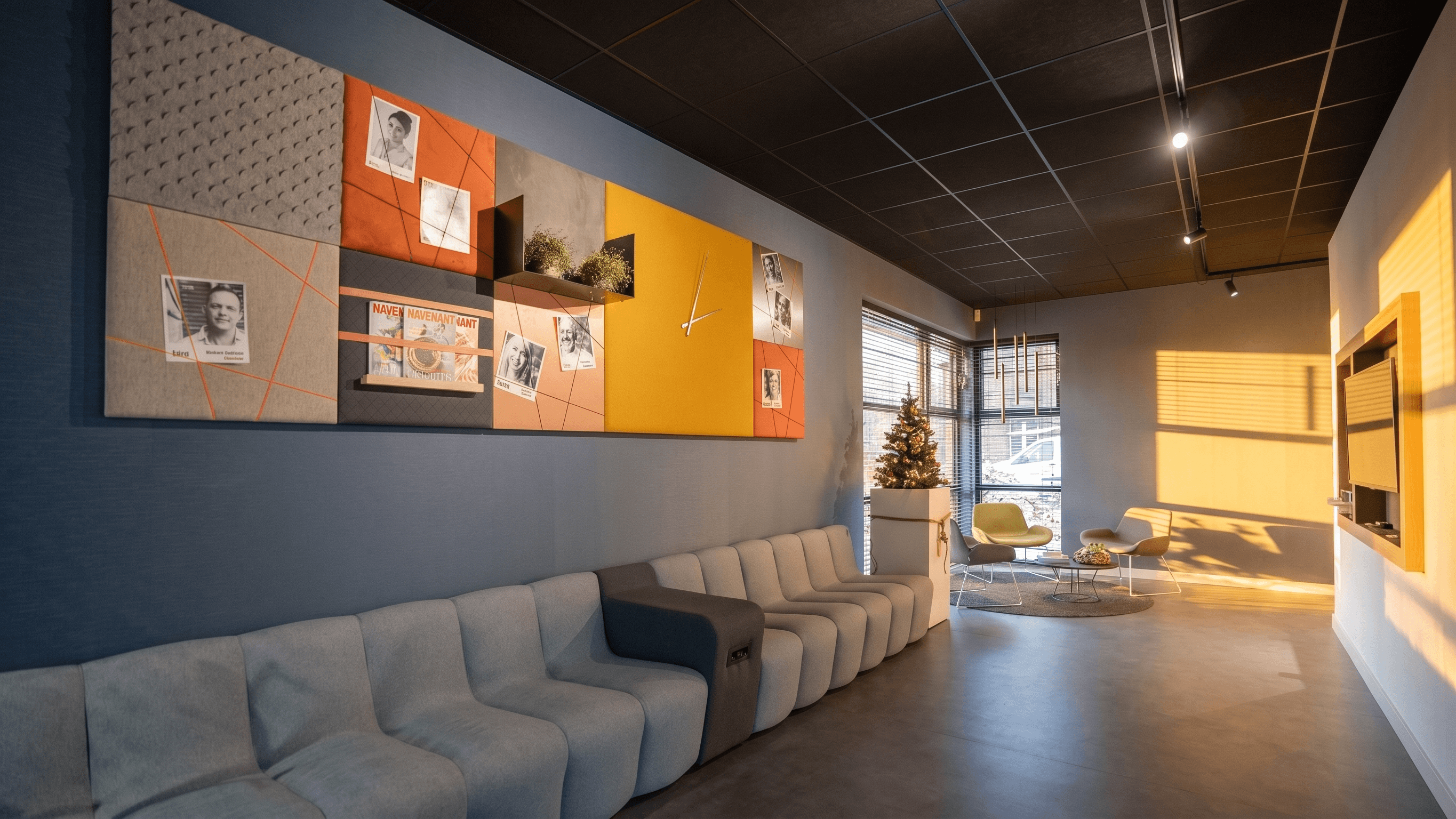 Wachtruimte met een modulaire loungebank, een groot akoestisch wandpaneel met kleurvlakken en portretten, afgestyled met warme sfeerverlichting.