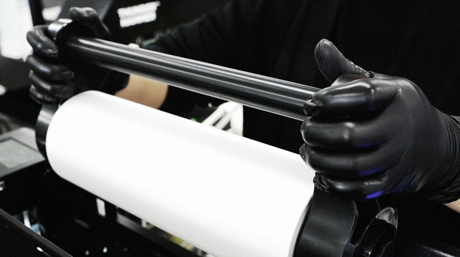 A worker wearing black gloves easily replacing the roll film using the Gravity Studio DTF printer's new feeding system for quick and stable operation
