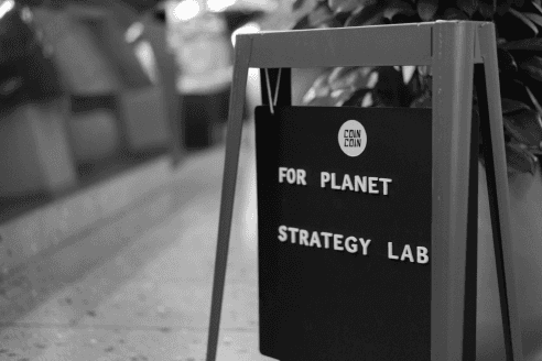 A black signboard displaying "For Planet Strategy Lab" placed on a sidewalk. The sign signifies the organization's commitment to regenerative value creation and integrating planetary perspectives into strategic initiatives.