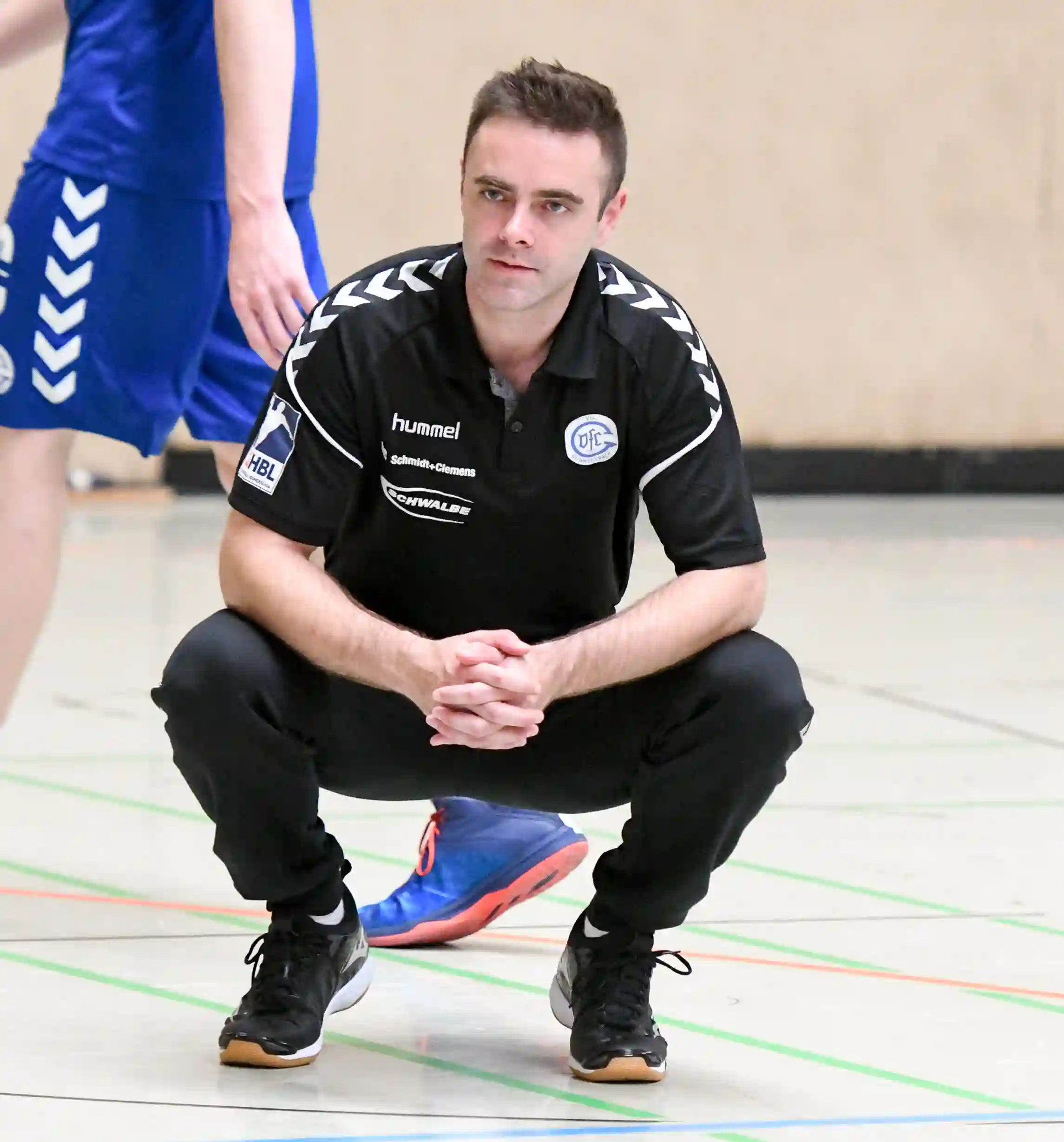A smiling woman with her arms crossed, standing against a dark green background. She has long, dark hair.