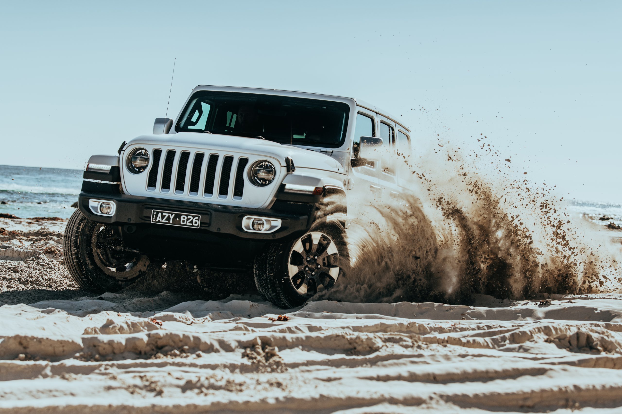 White four-wheel drive throwing up a wall of sand as it drives along a beach