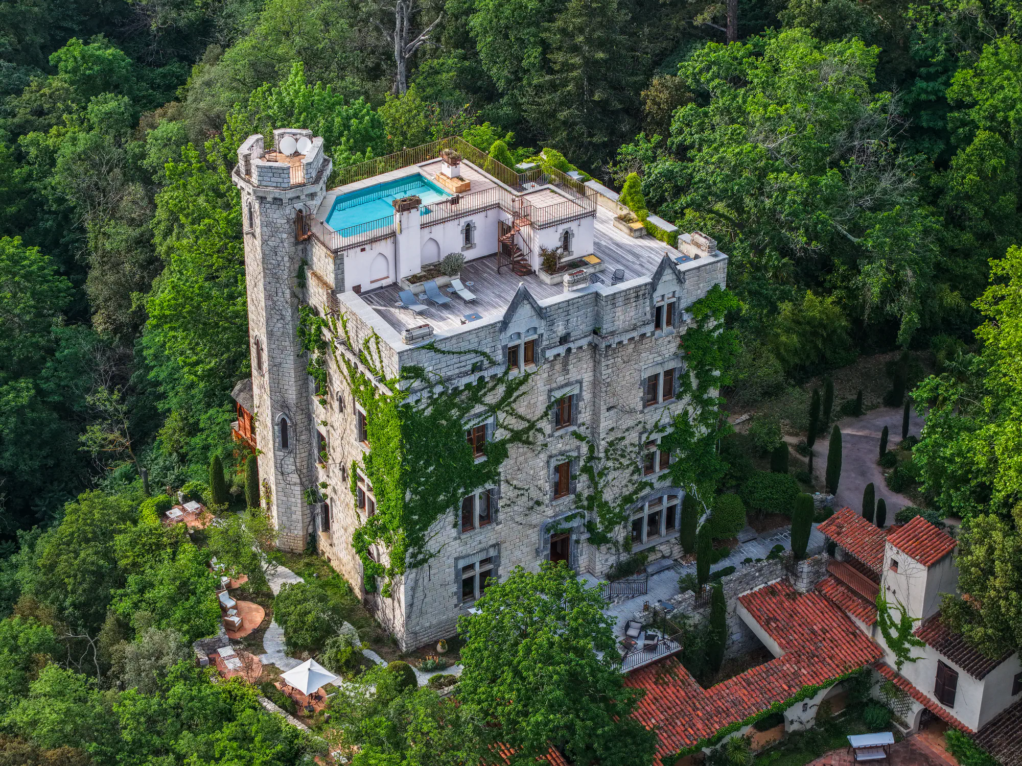 Vue aérienne d’un château couvert de lierre avec piscine sur le toit, au milieu de la forêt