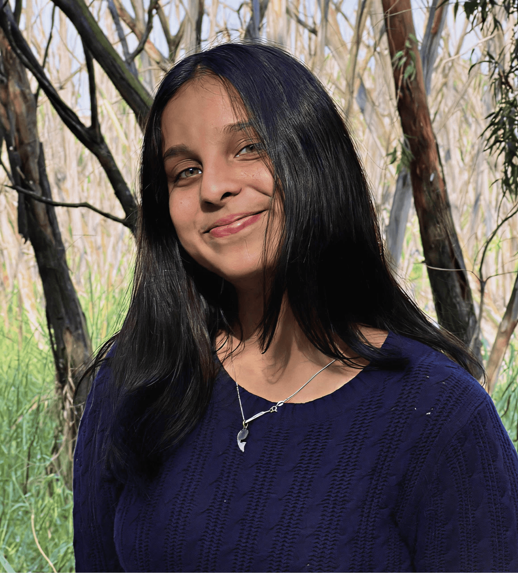 A young person with long, wavy hair sits in front of a plain background, looking directly at the camera.