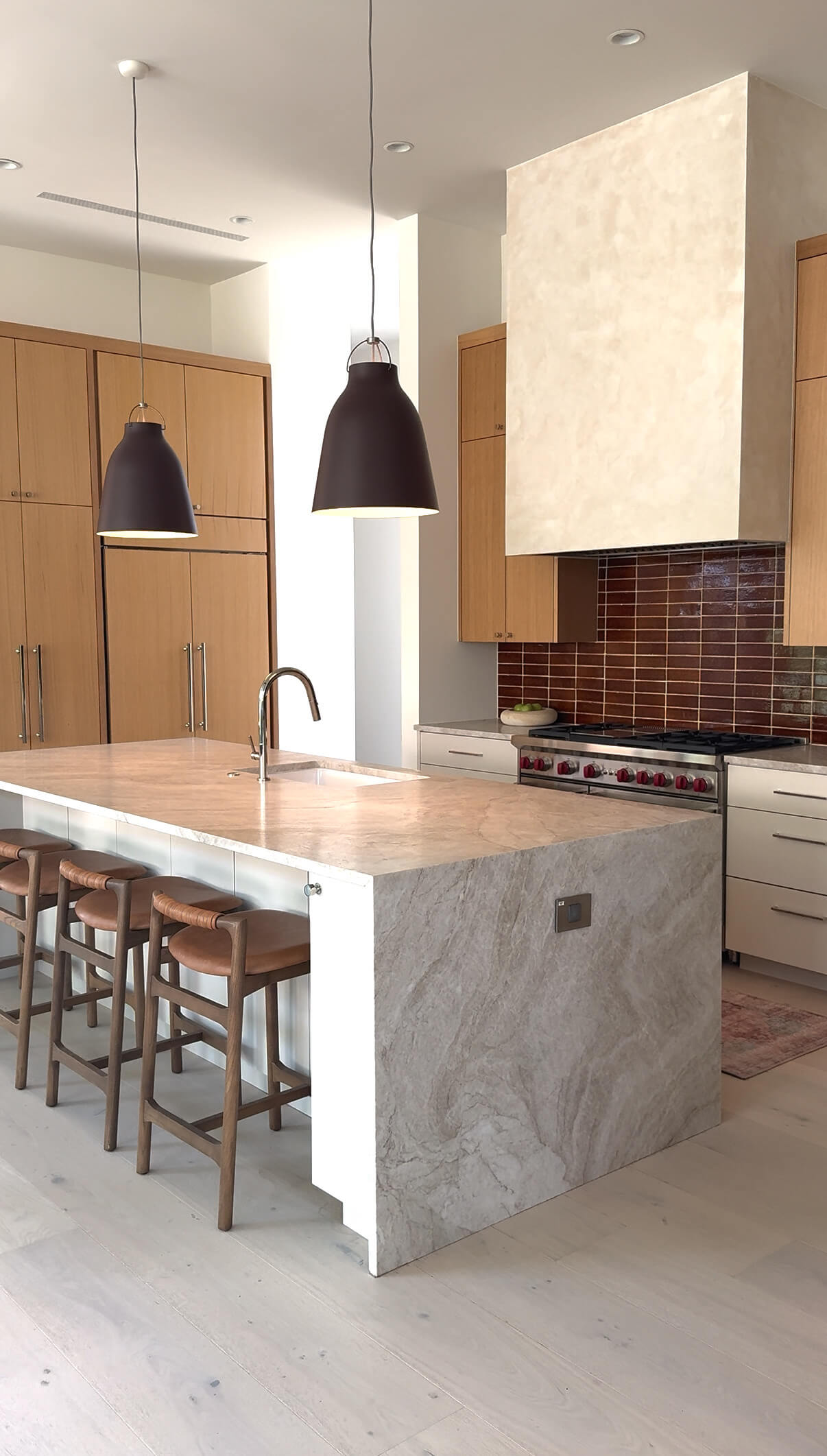 A modern kitchen with a marble waterfall island with an inset outlet and two drop lights hanging above the island.