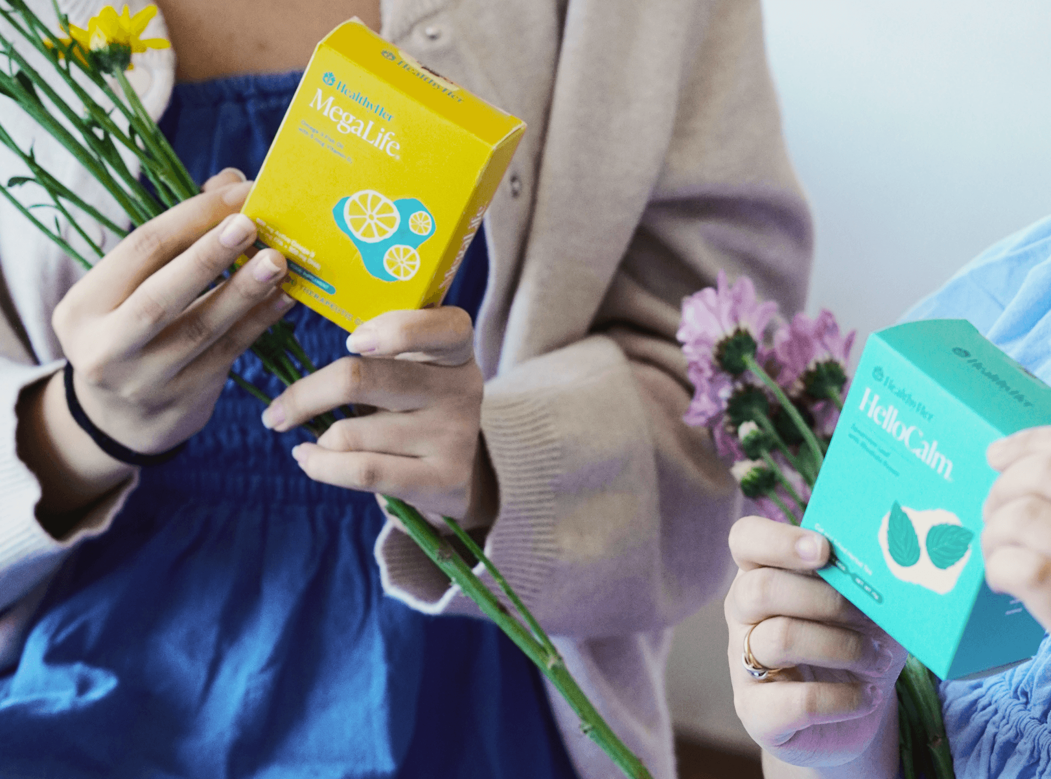 Two friends are holding boxes of Megalife and HelloCalm from HealthyHer