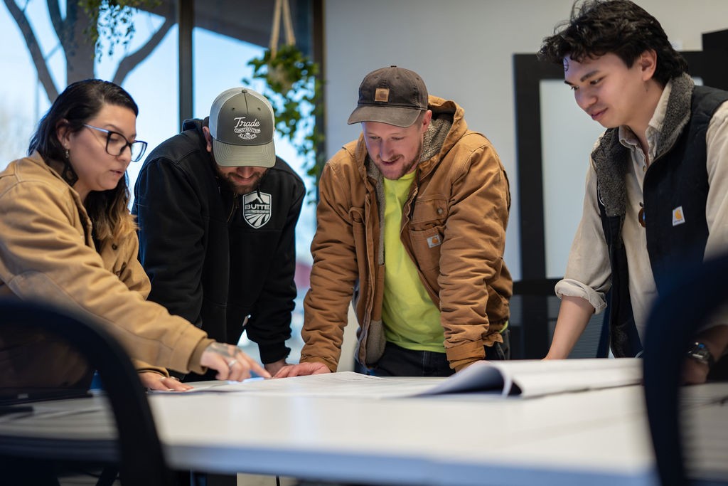 group of construction company employees standing around a conference room table reviewing building plans