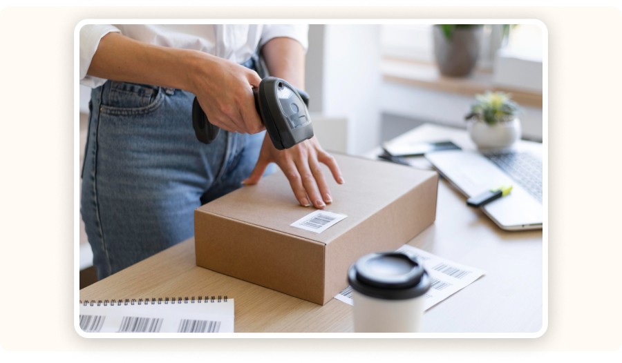 Person scanning barcode on package at desk with laptop and shipping labels