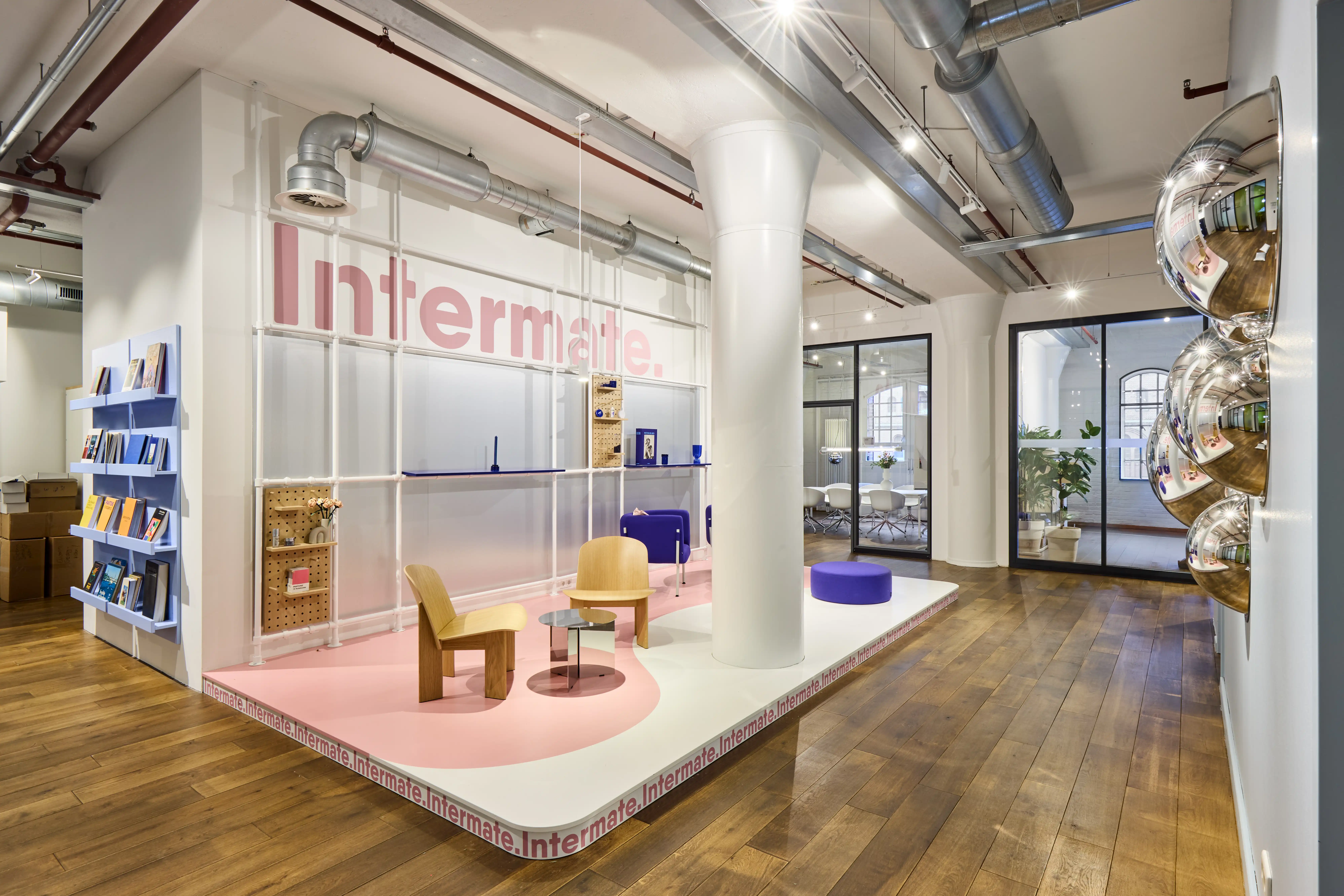 Open workspace at INTERMATE OFFICE HAMBURG with white height-adjustable desks, black office chairs, white-painted brick walls, three arched factory windows, and a birch shelving unit on wheels.