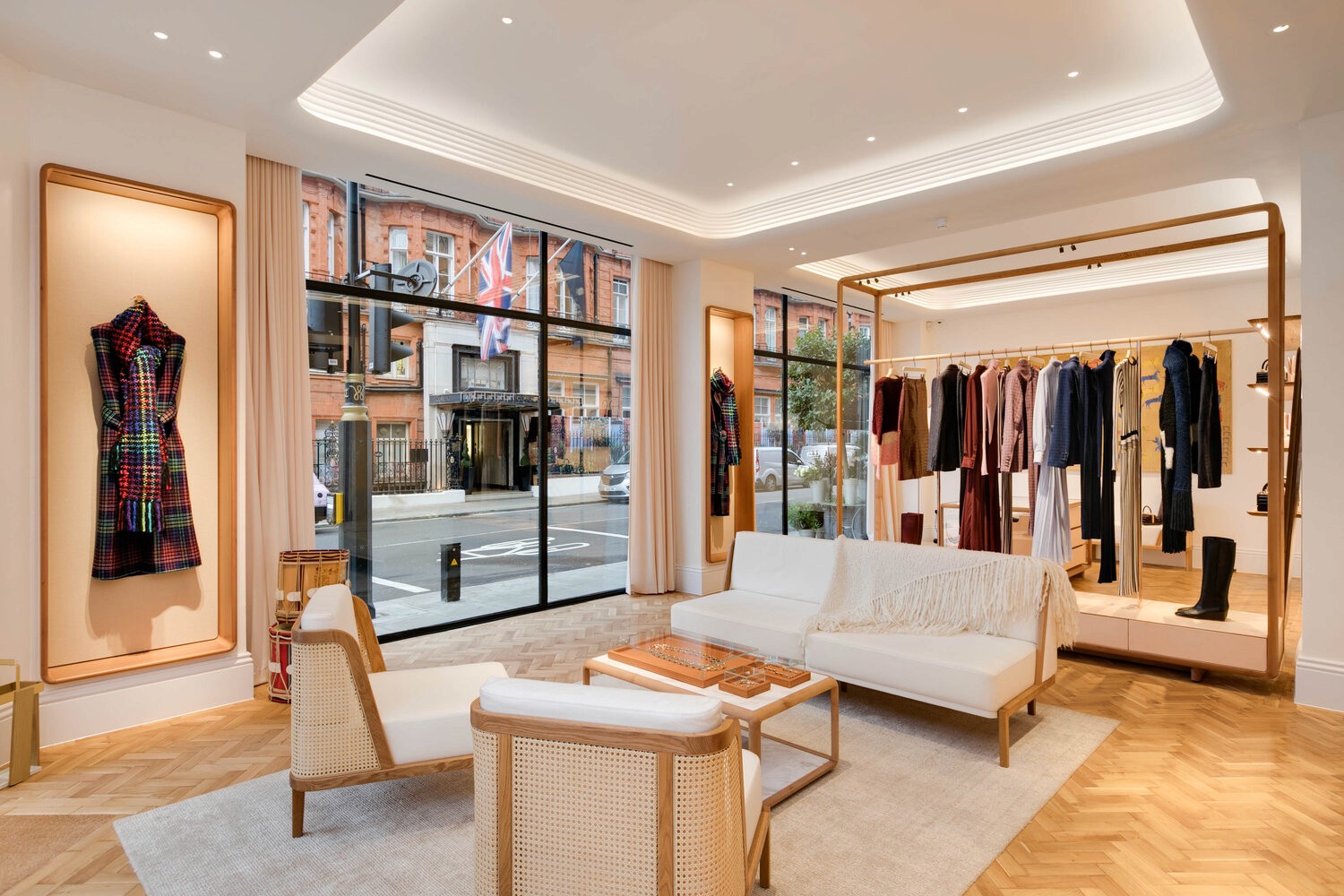 A luxury retail store showcasing a designer dress in a lit display, along with a modern seating area and large windows overlooking the street.