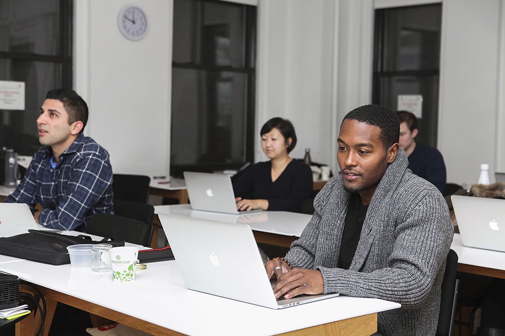 A designer sits at a desk in conversation, relaxed and professional..