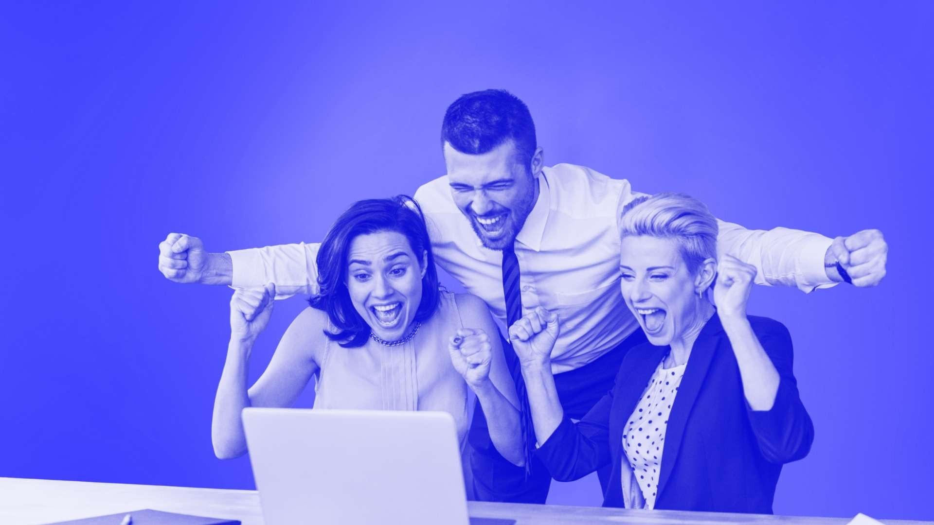 3 people in office attire sitting in front of a laptop celebrating a success with arms in the air