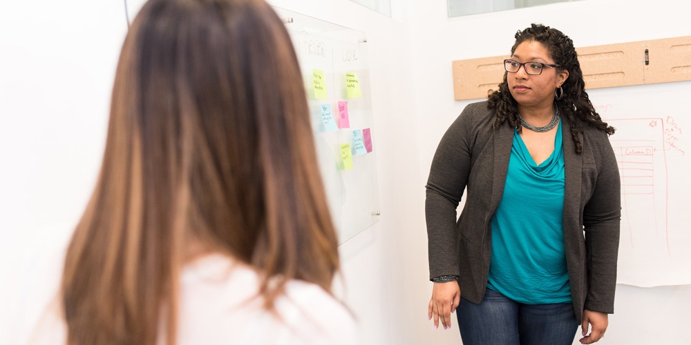 Two workshop participants looking at a whiteboard full of post-it notes.