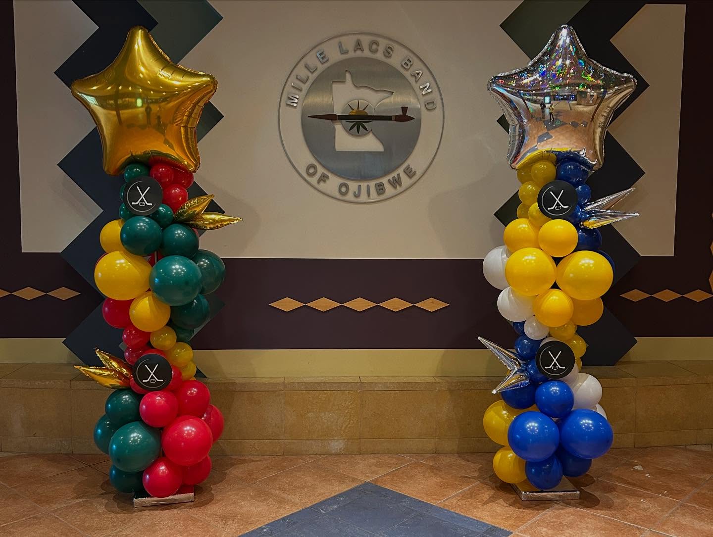 Gold star-topped balloon columns in red, blue, and yellow color scheme displayed indoors for an event by Be Bold Balloons