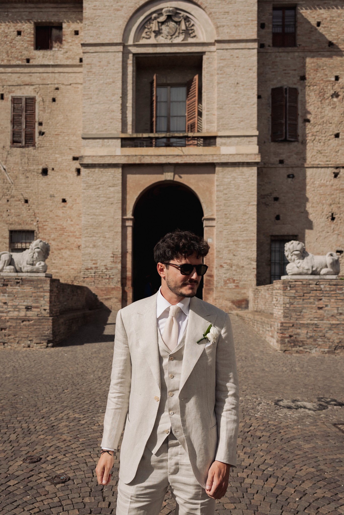 Bernardo in abito bianco avorio davanti alla Rocca di Soragna, ritratto matrimoniale nel cortile in luce naturale