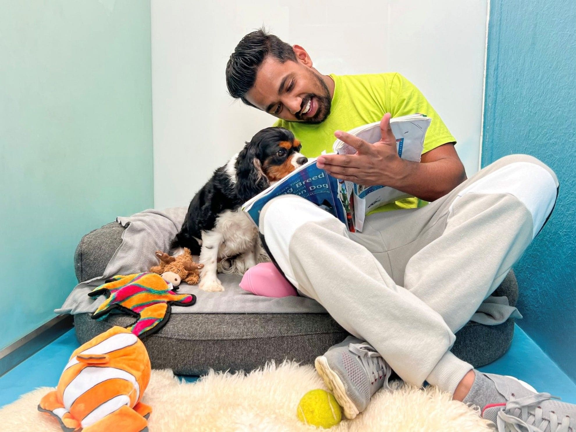 A pet attendant is sitting with a dog on a bed and reading a book.