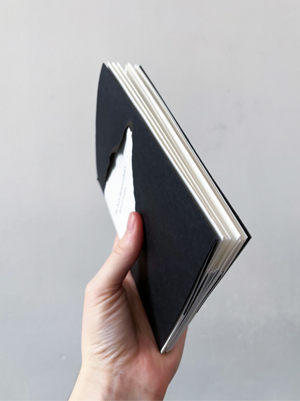 Een hand houdt een prototype van het boek vast. Dit beeld illustreert de kleine schaal en het fragiele, handzame karakter van het uiteindelijke boekobject.
