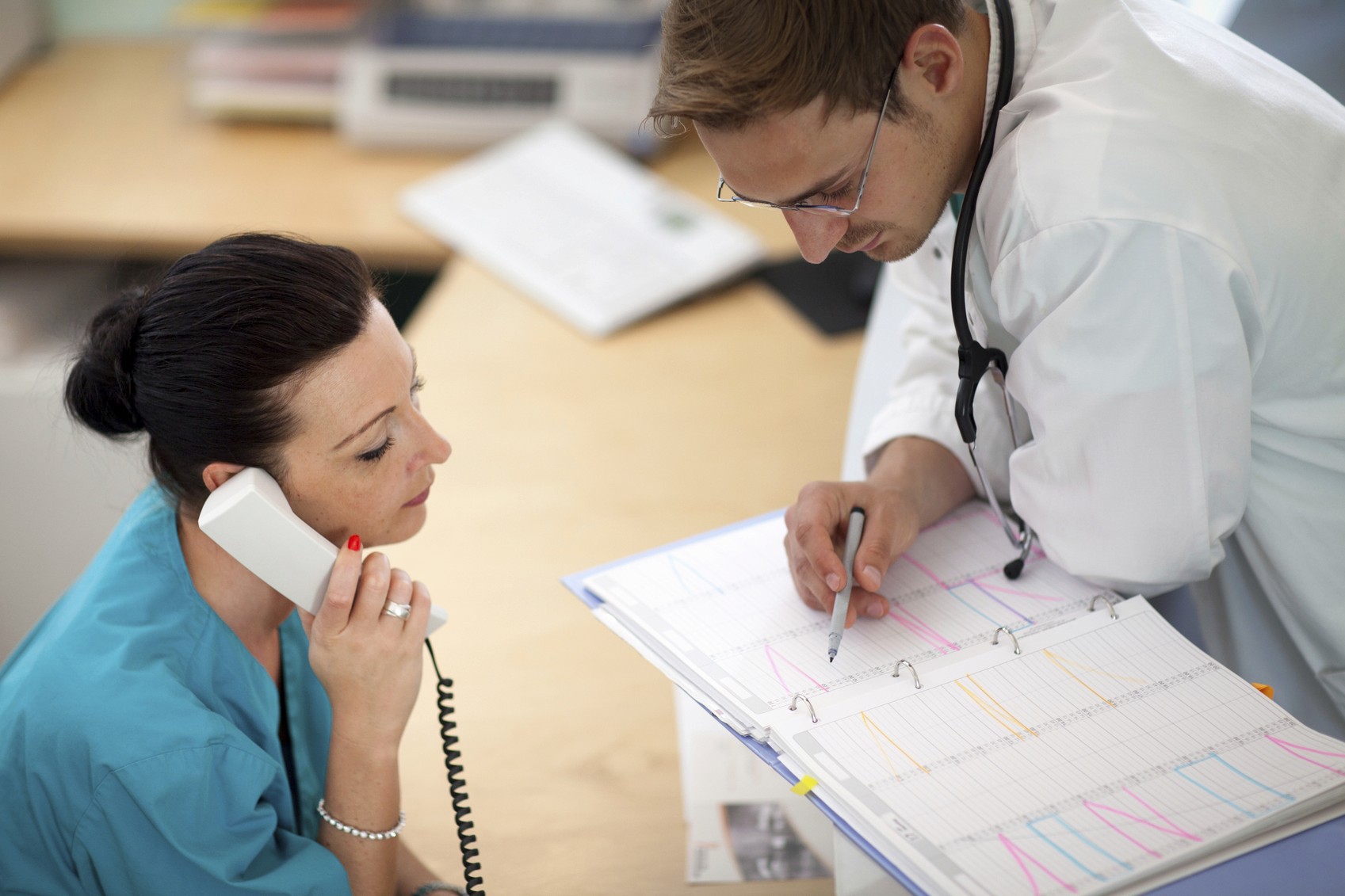 teamwork: young male doctor is looking into an organizer while his female assistant is listening at the phone