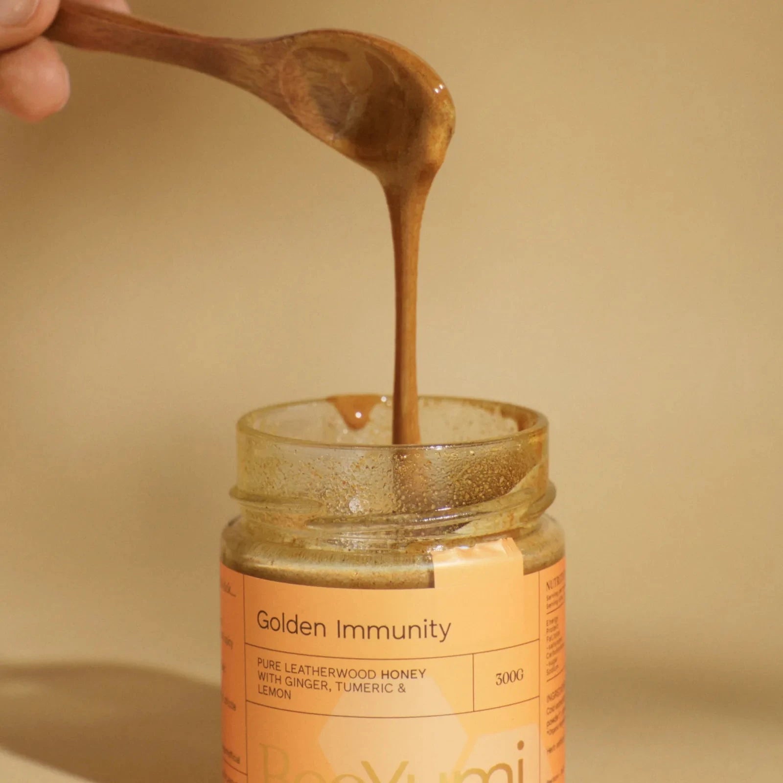 Jar of 'Golden Immunity' honey with a wooden spoon lifting some honey, on a beige background.