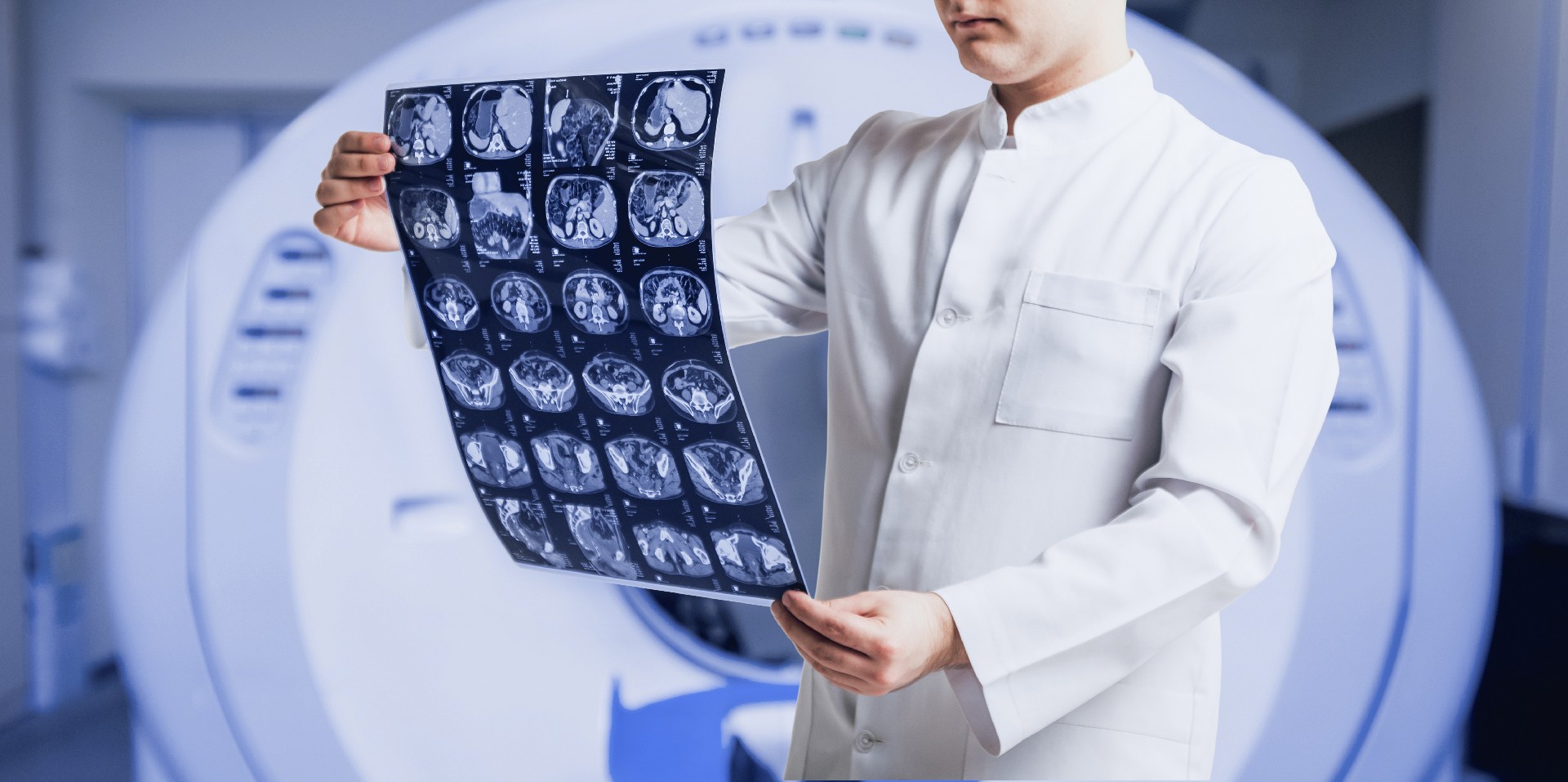 A doctor examines MRI scans in front of an MRI machine. The setting is clinical, focusing on medical analysis and diagnostics.