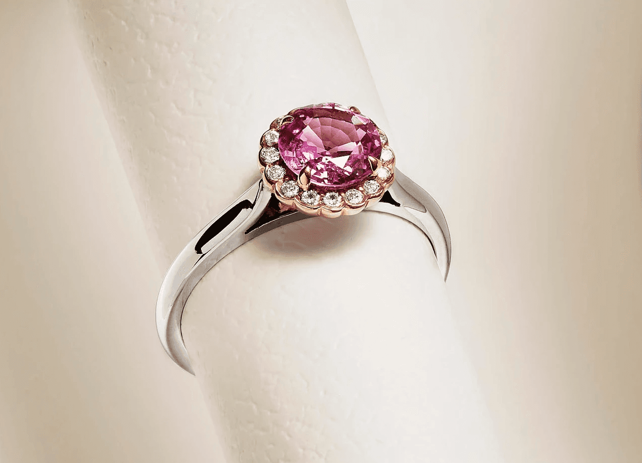 A silver ring with a pink gemstone in a polished setting, displayed on a soft, light background.