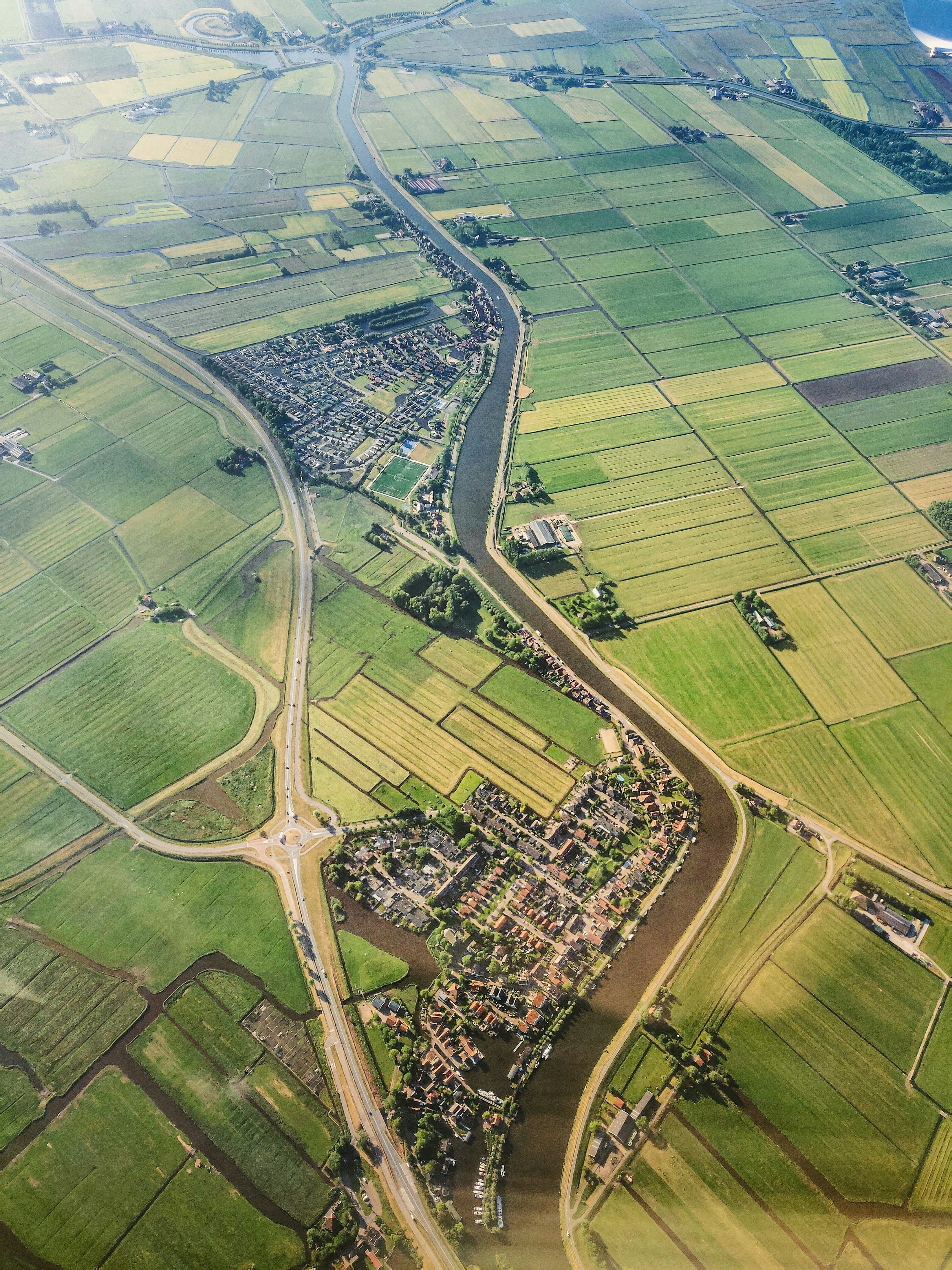 Luchtfoto van het Nederlandse polderlandschap: groene/gele rechthoekige velden, doorsneden door een kanaal en wegen, met t...