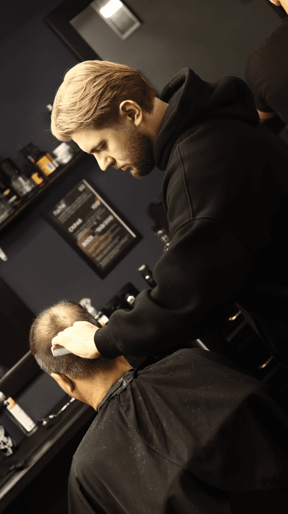 A barber styles a client's hair in a well-lit salon, focused on creating a precise look.