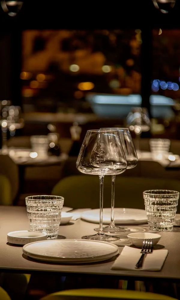 Table dressée de verres à vin au bord des baies vitrées, le soir
