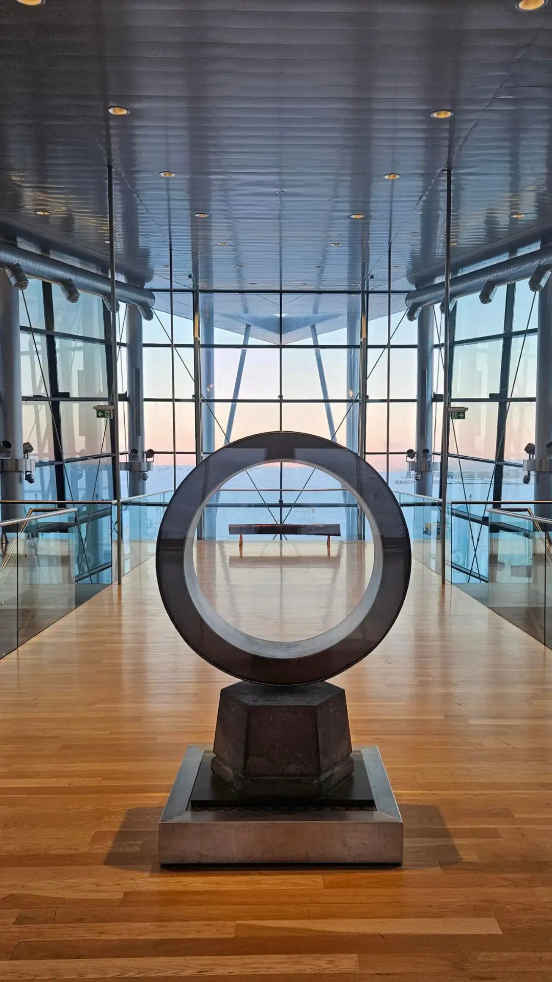 A person in an orange jacket standing on a geothermal facility platform with pipes and snowy mountains in the background
