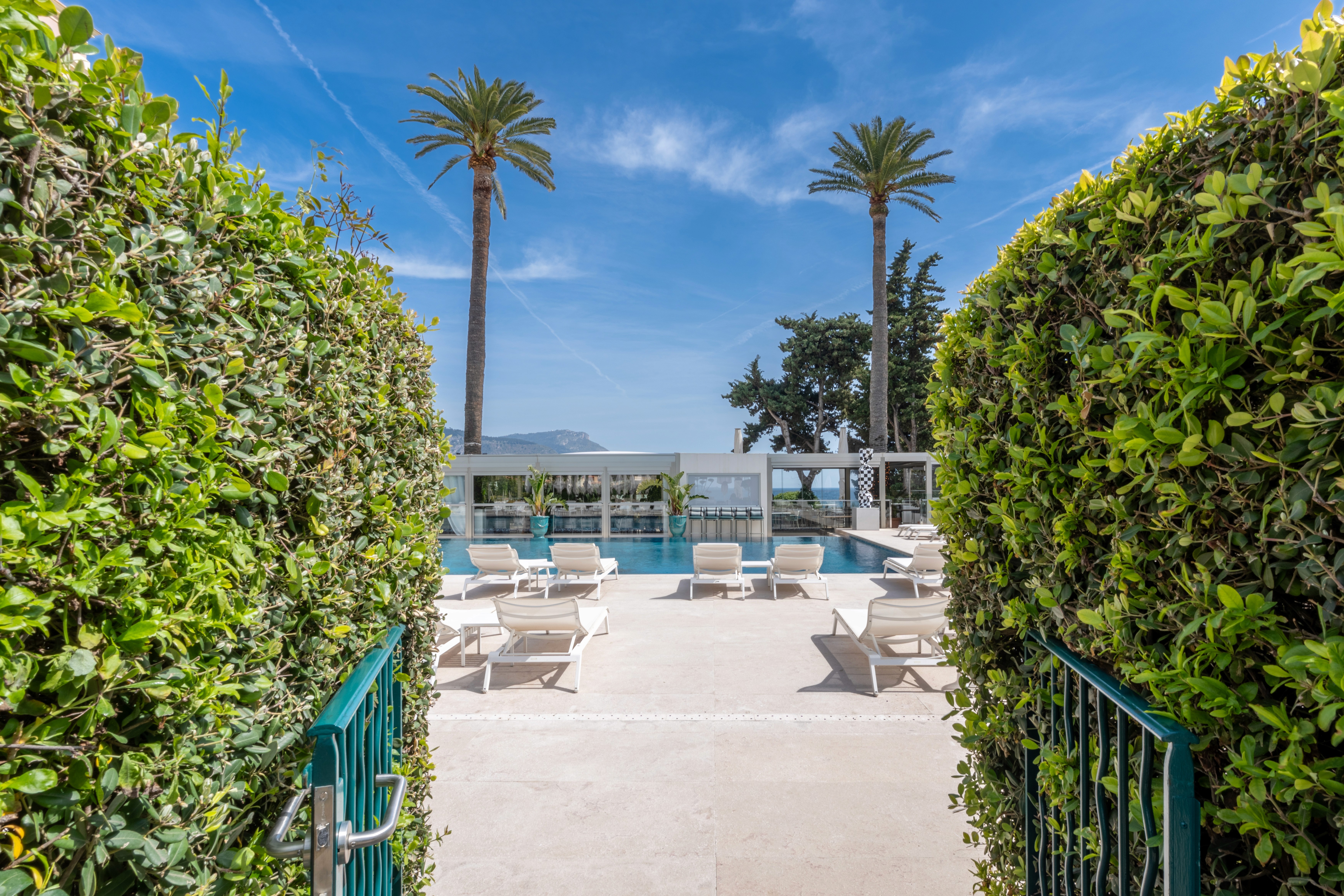 Entrance to outdoor pool at Royal Riviera Hotel framed by hedges and palm trees on the French Riviera