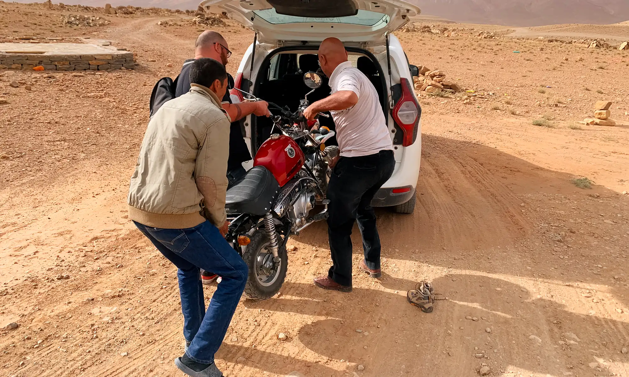 Three men lifting a motorcycle into the back of a white van.