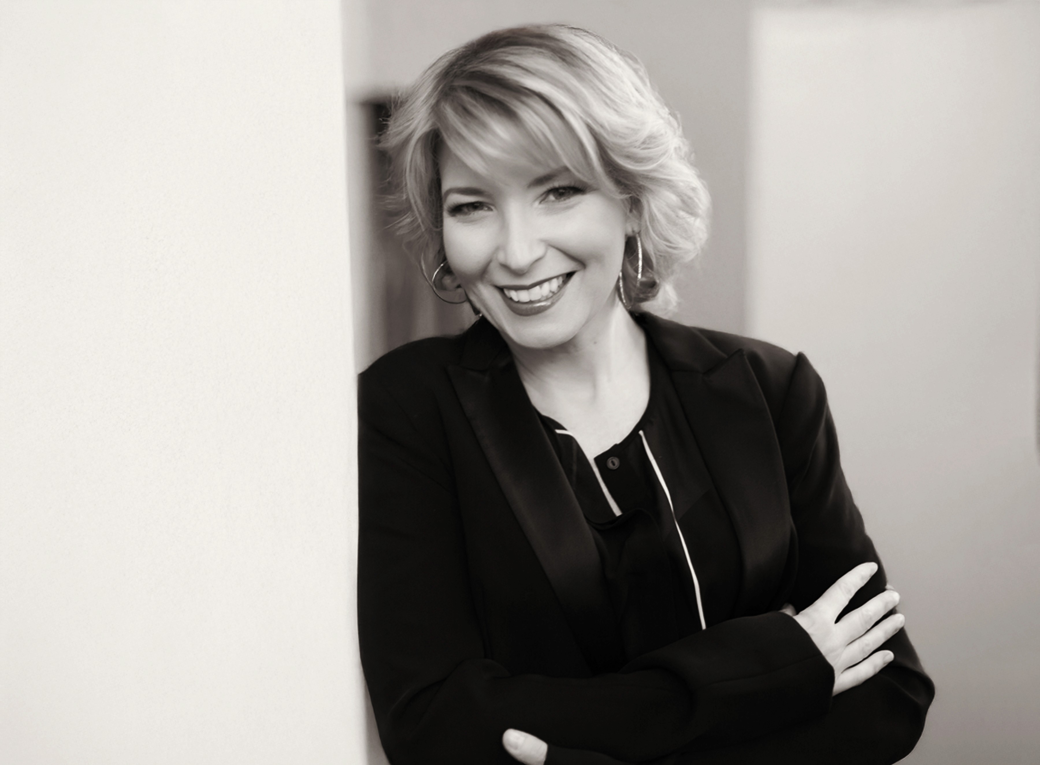 Black and white photo of executive and organizational consultant Cheryl Carreau, leaning against a white wall, smiling and wearing a black blazer.