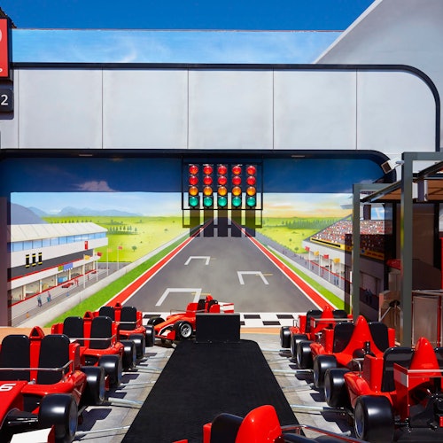 A row of red racing car seats in front of a large race track mural, complete with a detailed finish line and a traffic light.