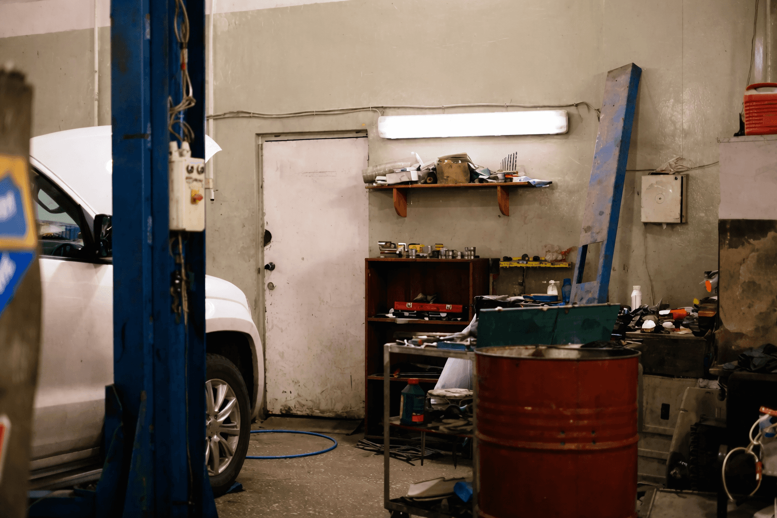 Auto repair workshop interior with tools, shelves, a red barrel, and part of a white car.
