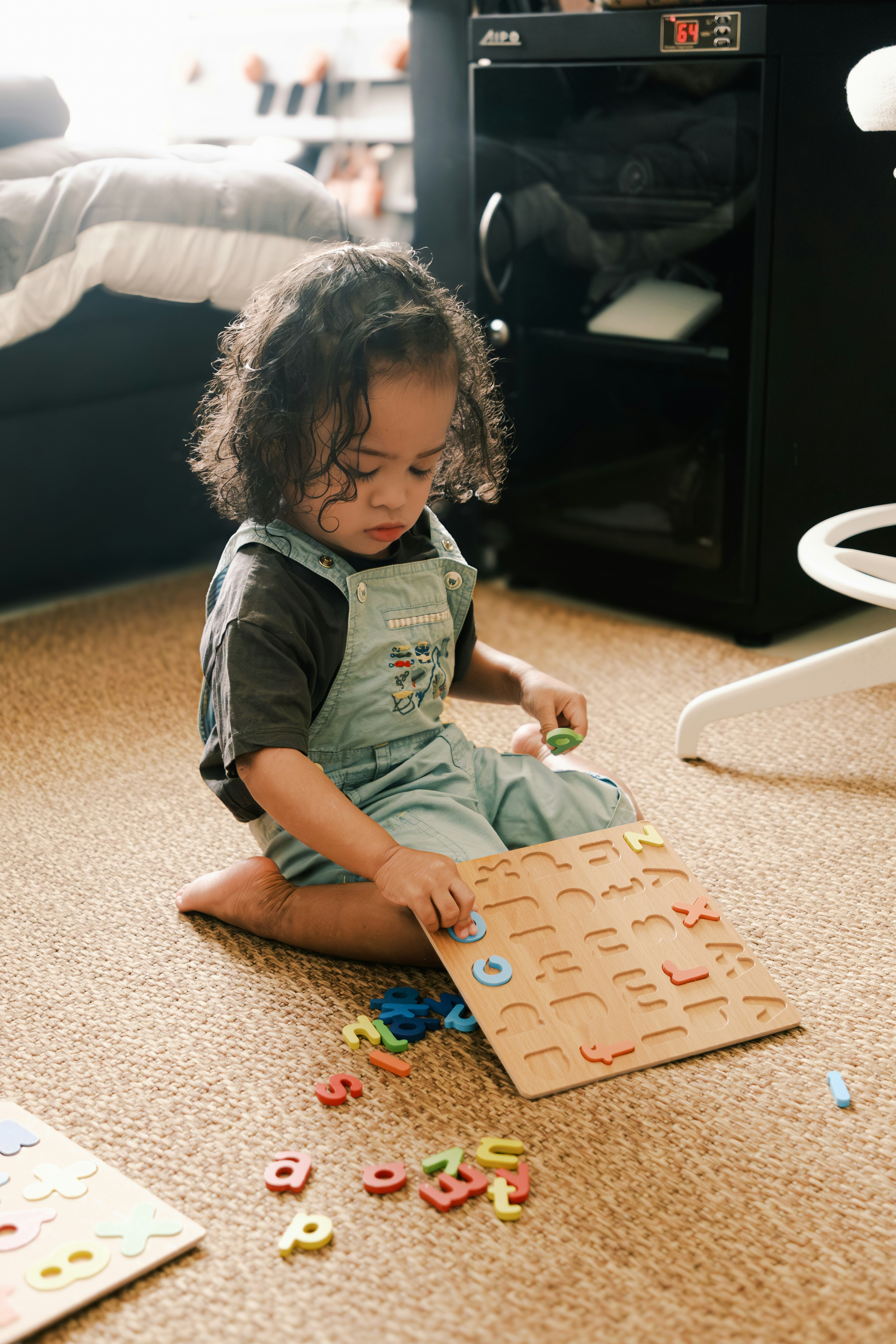 Young child plays with alphabet puzzle on floor.