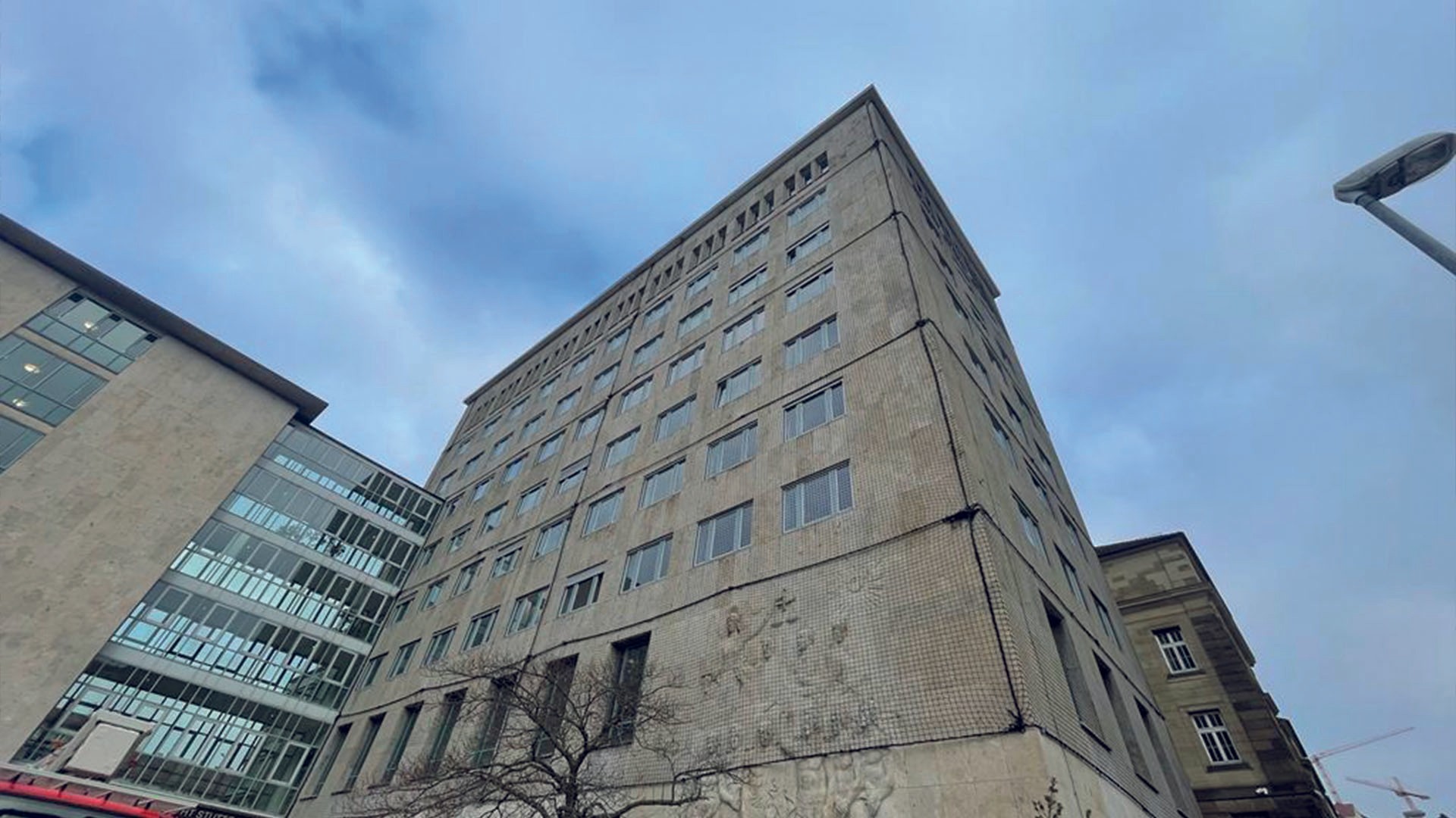 Woman in glasses and business-casual attire smiling confidently while standing in an office space with a corkboard in the background.